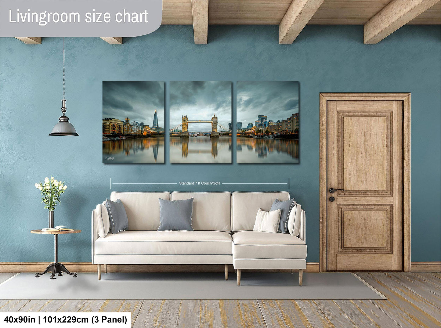 The image is a living room with a large, three-panel wall art depicting a cityscape with a bridge in the background. The wall art is mounted above a white sofa, and there is a wooden door and a small table with a vase of flowers nearby. The living room appears to be well-lit and spacious, with a wooden floor and a blue wall.