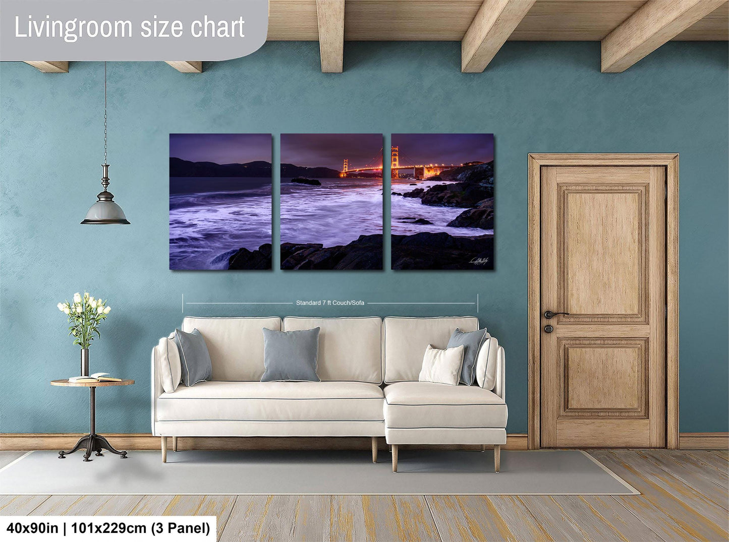 The image is a living room with a large wall art piece depicting a scenic view of the Golden Gate Bridge at night. The art piece is divided into three panels, each showing different aspects of the bridge and the surrounding landscape. The living room has a white sofa and a wooden door, creating a cozy and inviting atmosphere.
