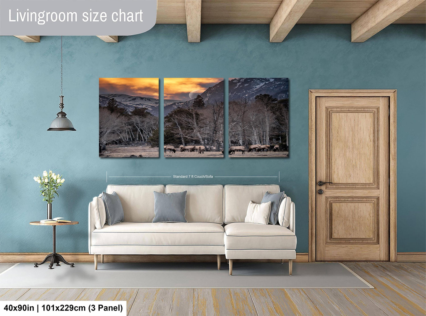 The image is a living room with a large, three-panel landscape painting hanging on the wall. The painting depicts a snowy mountain scene with a sunset. The room has a white sofa and a wooden door, and there is a vase of flowers on a table. The painting is approximately 40 inches wide and 101.29 cm tall, with a 3-panel layout.