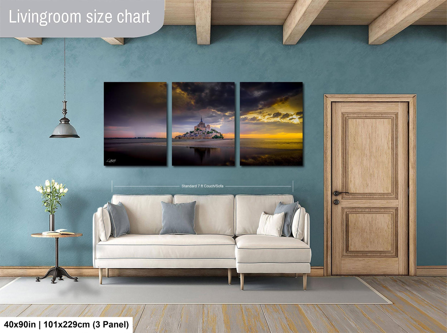 The image is a living room with a white sofa and a wooden door. Above the sofa, there is a triptych of landscape paintings depicting a sunset over a body of water. The paintings are framed and hung on the wall.