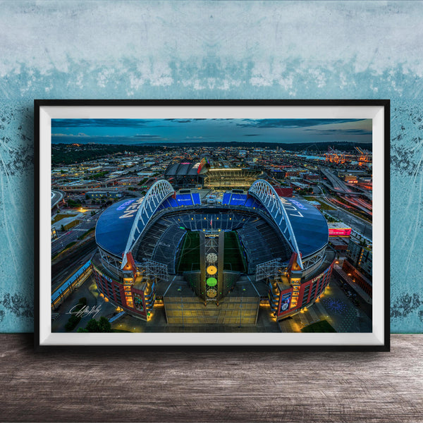 The image is a framed photograph of a large stadium at night, with the stadium's lights illuminating the surrounding cityscape.