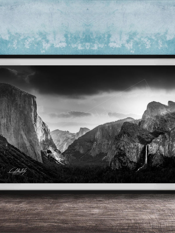 A black and white photograph of a mountainous landscape, with dramatic clouds and a waterfall in the foreground.