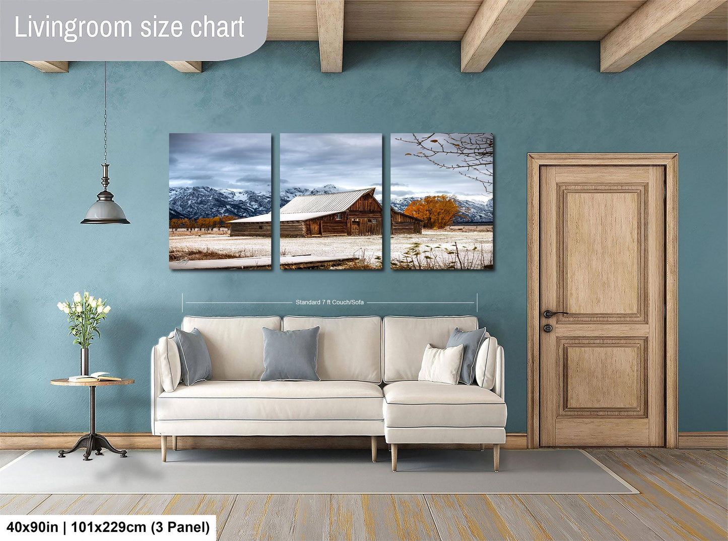 The image is a living room with a large wall art depicting a winter landscape with a barn and mountains. The living room has a white sofa and a wooden door.