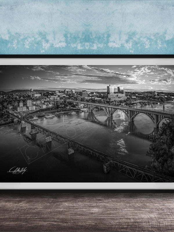 A black and white aerial photograph of a cityscape with a large bridge spanning a river, set against a blue textured wall.
