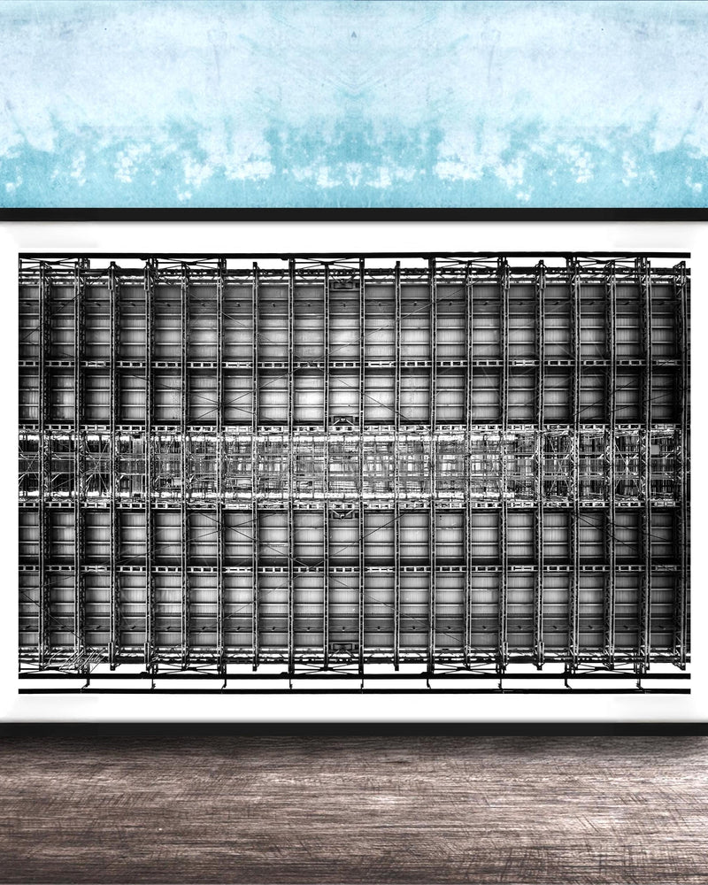 The image is a framed black and white photograph of a grid-like structure, possibly a building or a machine, set against a blue textured wall.