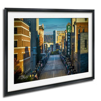 a city street lined with tall buildings, including a prominent sign for "TENNESSEE" on the right side. The street is decorated with numerous American flags, suggesting a patriotic or celebratory atmosphere. The overall scene conveys a sense of community and pride in the city.