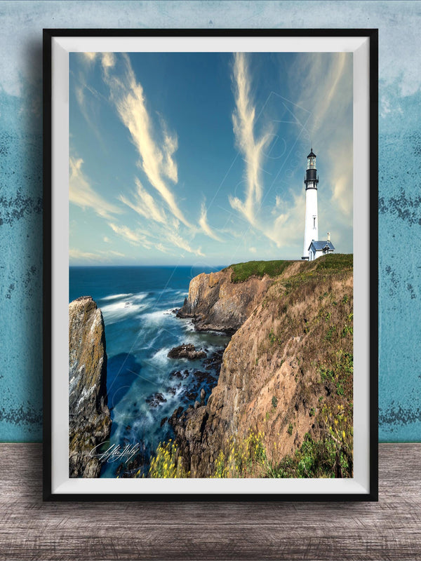A framed photograph of a lighthouse on a cliff overlooking the ocean, with a blue sky and wispy clouds in the background.