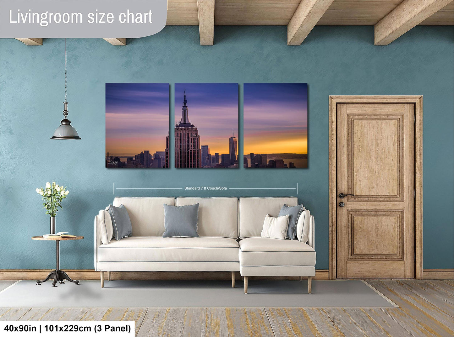 The image is a living room with a large wall-mounted painting depicting the New York City skyline at sunset. The painting is divided into three panels, with the top and bottom panels showing the cityscape and the middle panel showing the sky. The painting is framed in a standard size of 71.5 x 101.25 cm (3 panel).