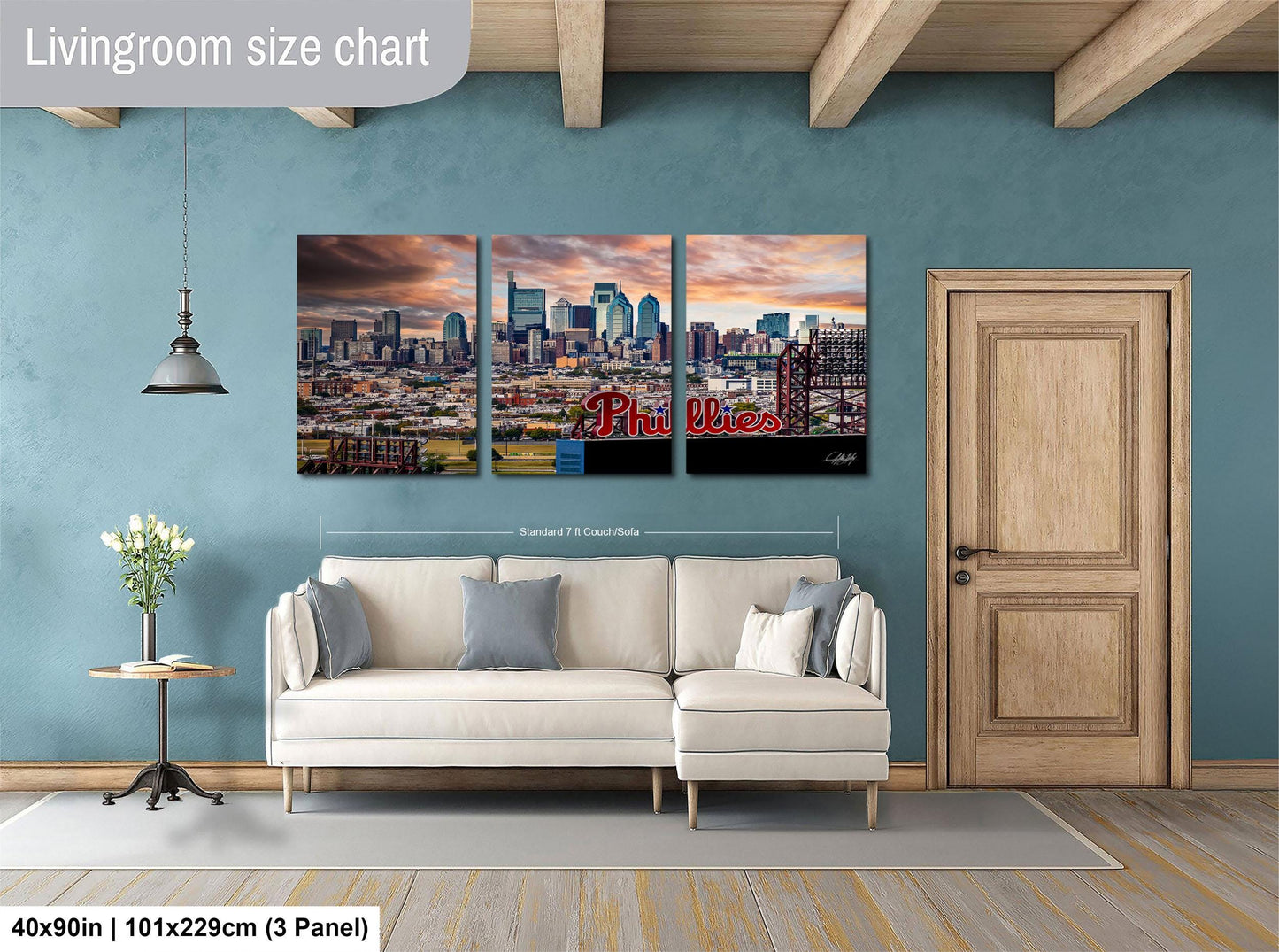 The image is a living room with a large wall art depicting a city skyline, a white sofa, a wooden door, and a small table with a vase of flowers.