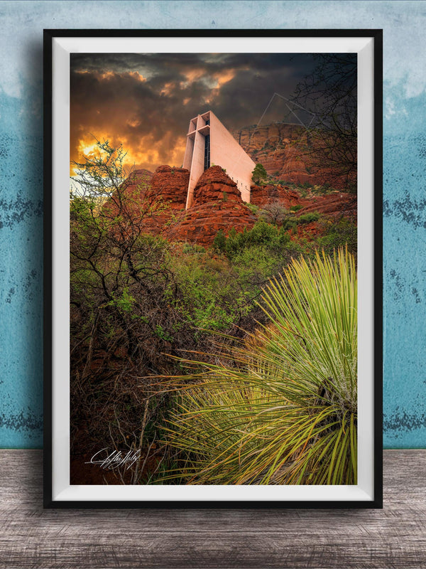 a framed photograph of a desert landscape with a large, white structure in the background, possibly a building or monument, set against a dramatic sky with clouds and a sunset.