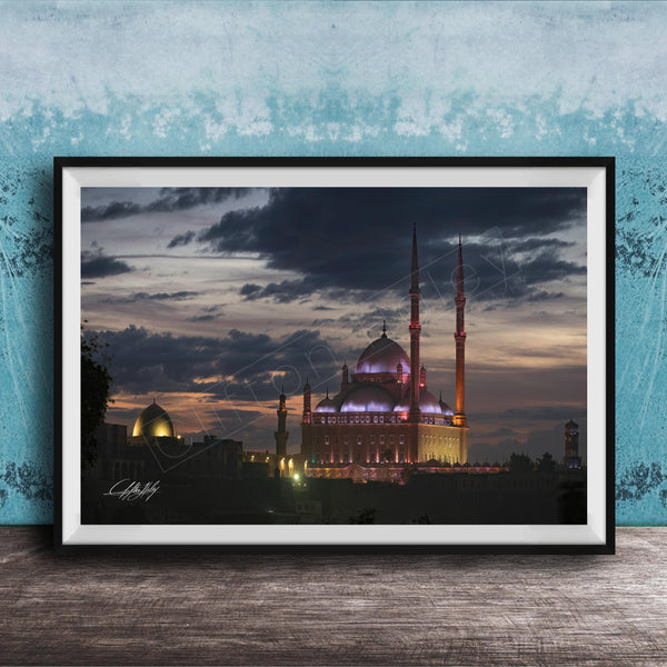 A framed photograph of a mosque at night, with its illuminated domes and minarets standing against a dark sky with clouds.