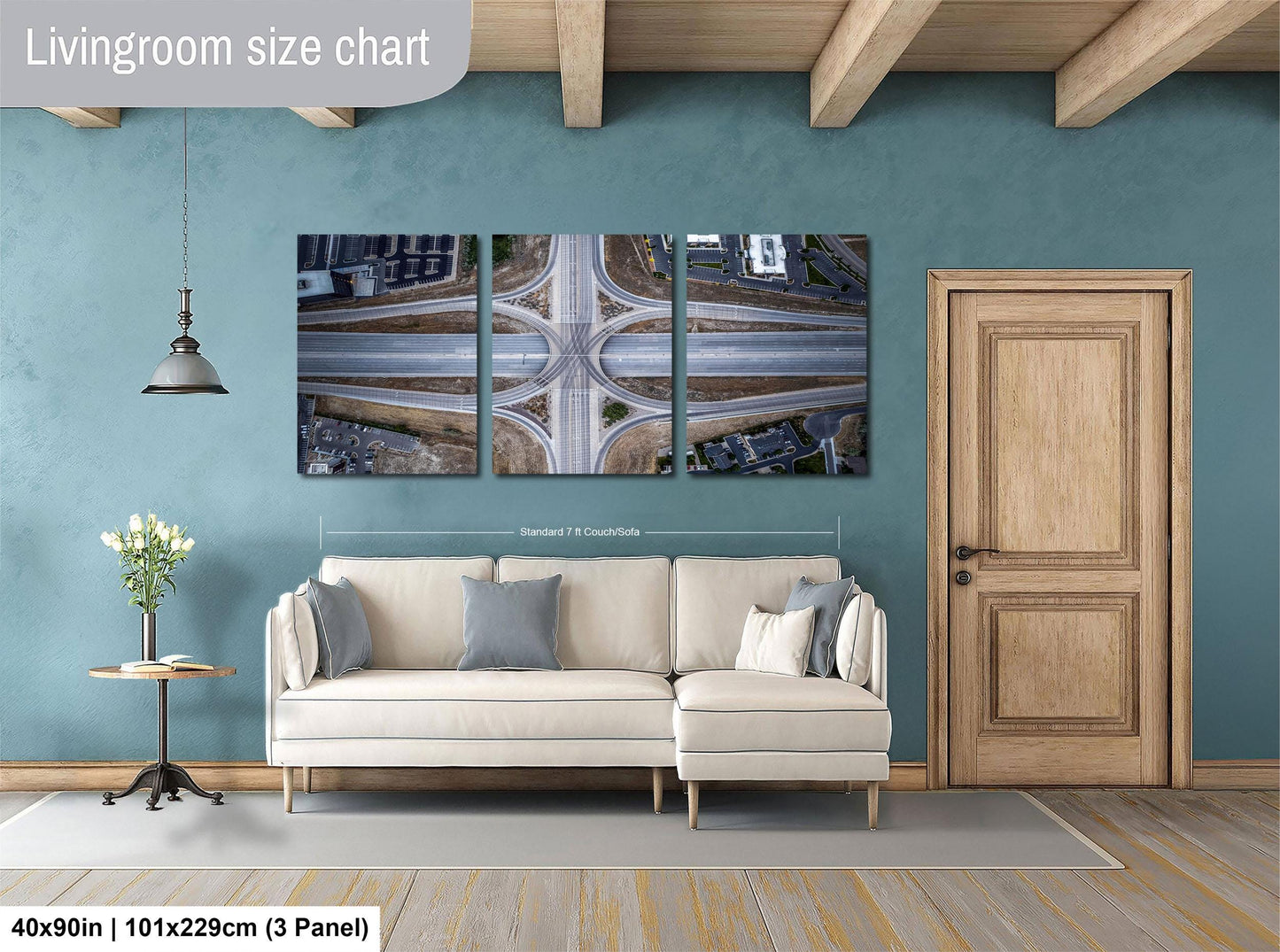 The image is a living room with a large white sofa, a wooden door, and a hanging light fixture. Above the sofa, there is a large wall art collage depicting an aerial view of a highway intersection.