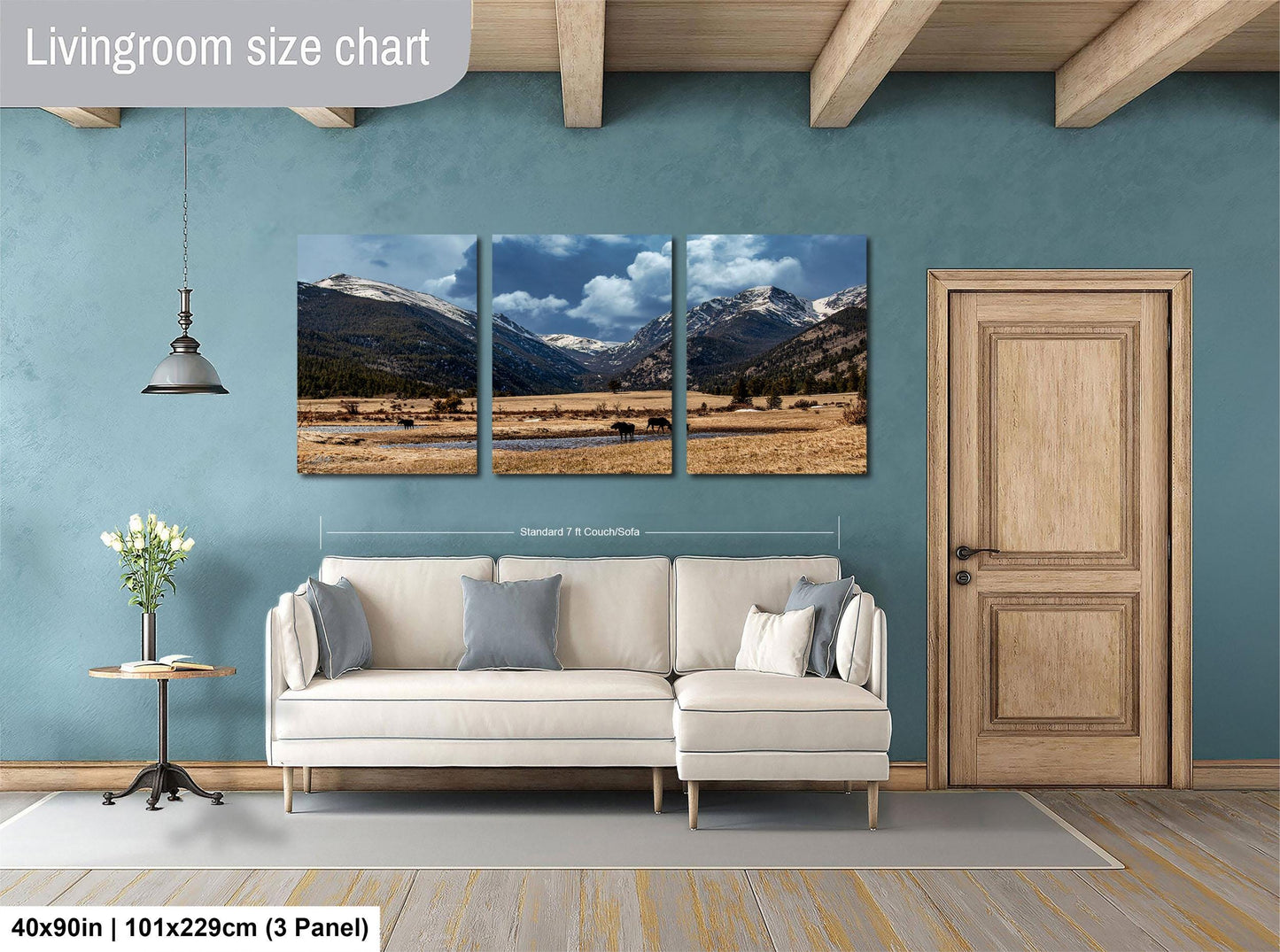 The image is a living room with a large wall art depicting a scenic mountain landscape. The wall art is divided into three panels, each showing a different part of the mountain range. The living room has a white sofa and a wooden door, creating a cozy and inviting atmosphere.
