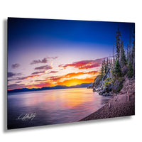 a serene sunset over a calm lake, with a rocky shoreline and trees in the foreground.