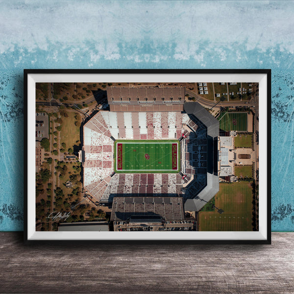 The image is an aerial view of a football stadium with a green field and surrounding buildings.