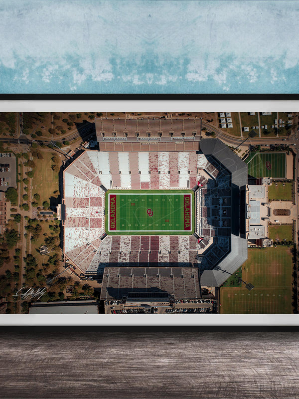 The image is an aerial view of a football stadium with a green field and surrounding buildings.
