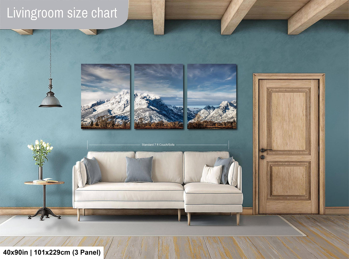 The image is a living room with a large wall art depicting a scenic mountain landscape. The wall art is composed of three panels, each showing a different view of the mountain range. The living room has a white sofa and a wooden door, creating a cozy and inviting atmosphere.