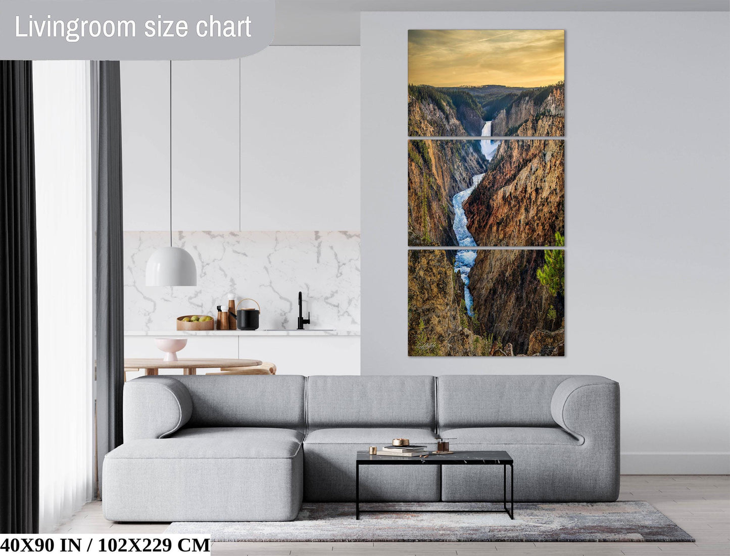 The image is a living room with a gray sofa and a coffee table in front of it. Above the sofa, there is a large painting depicting a waterfall in a mountainous landscape. The painting is framed and hangs on the wall.