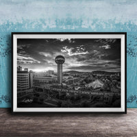A black and white photograph of a cityscape, featuring a tall tower, a bridge, and other buildings, set against a cloudy sky.
