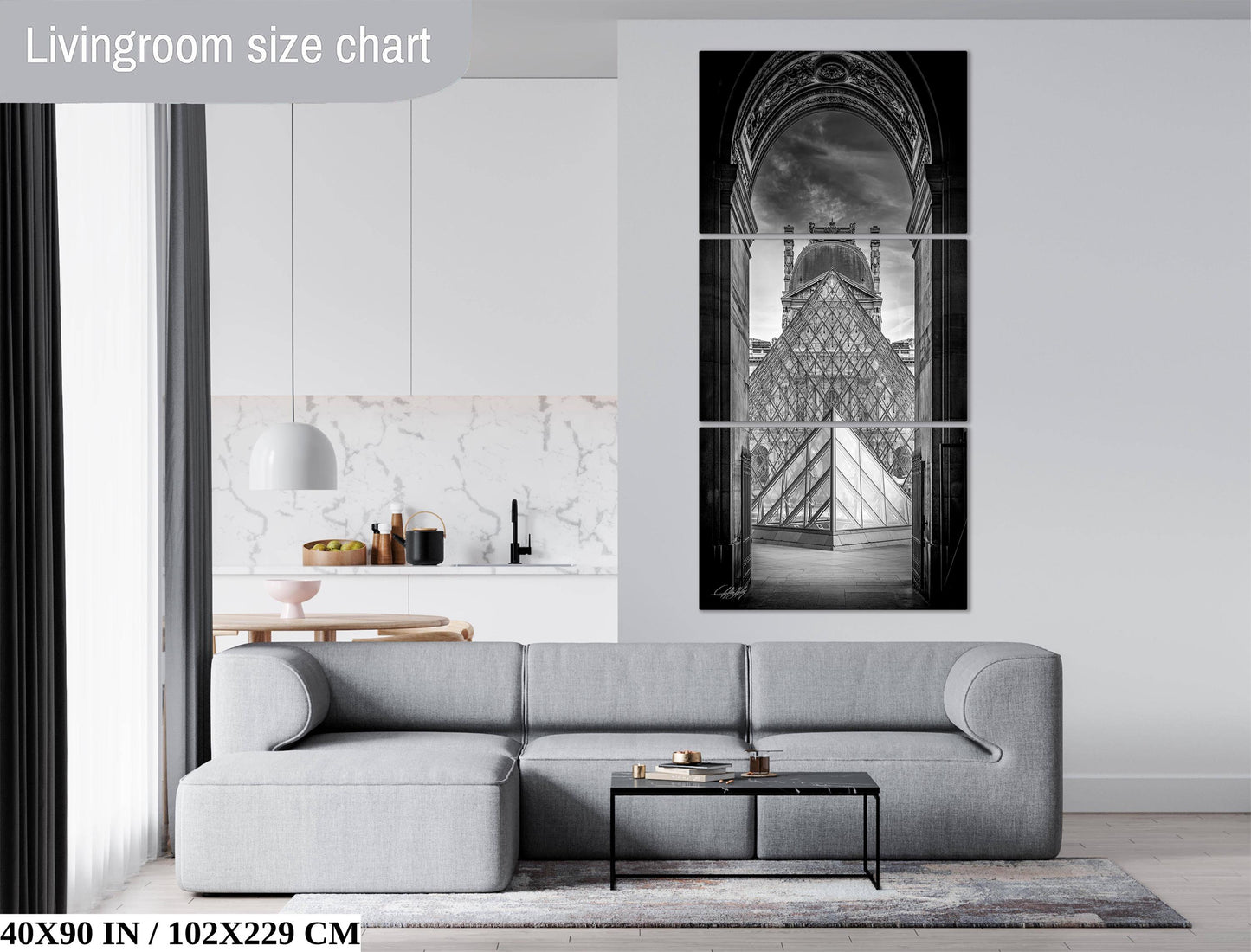 The image is a living room with a gray sofa, a coffee table, and a large black and white photograph of the Louvre Museum displayed on the wall.