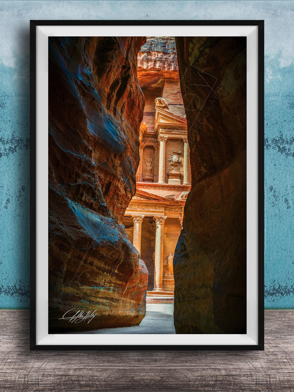 A framed photograph of a narrow passage between two large rock formations, with a building visible through the opening.