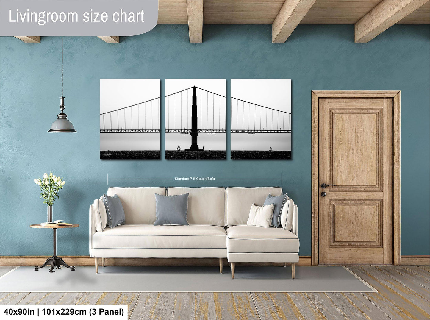 The image is a living room with a large white sofa, a wooden door, and a wall with a large black and white photograph of a suspension bridge.