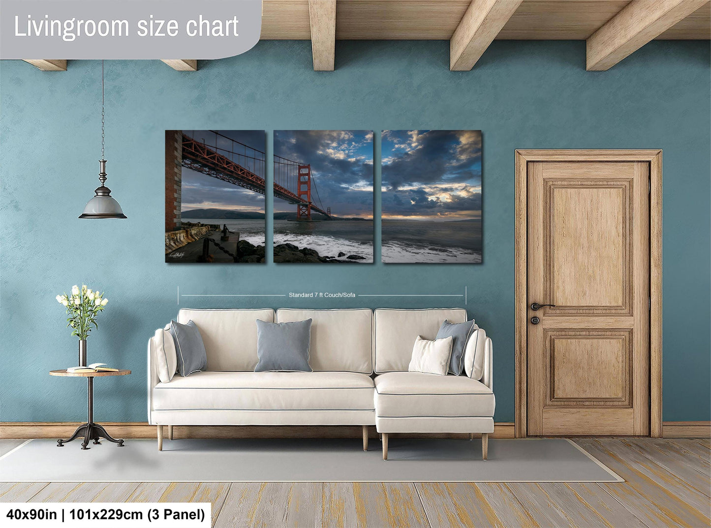 The image is a living room with a large wall art depicting the Golden Gate Bridge. The wall art is divided into three panels, each showing different parts of the bridge. The living room has a white sofa and a wooden door, and the floor is covered with a gray rug.