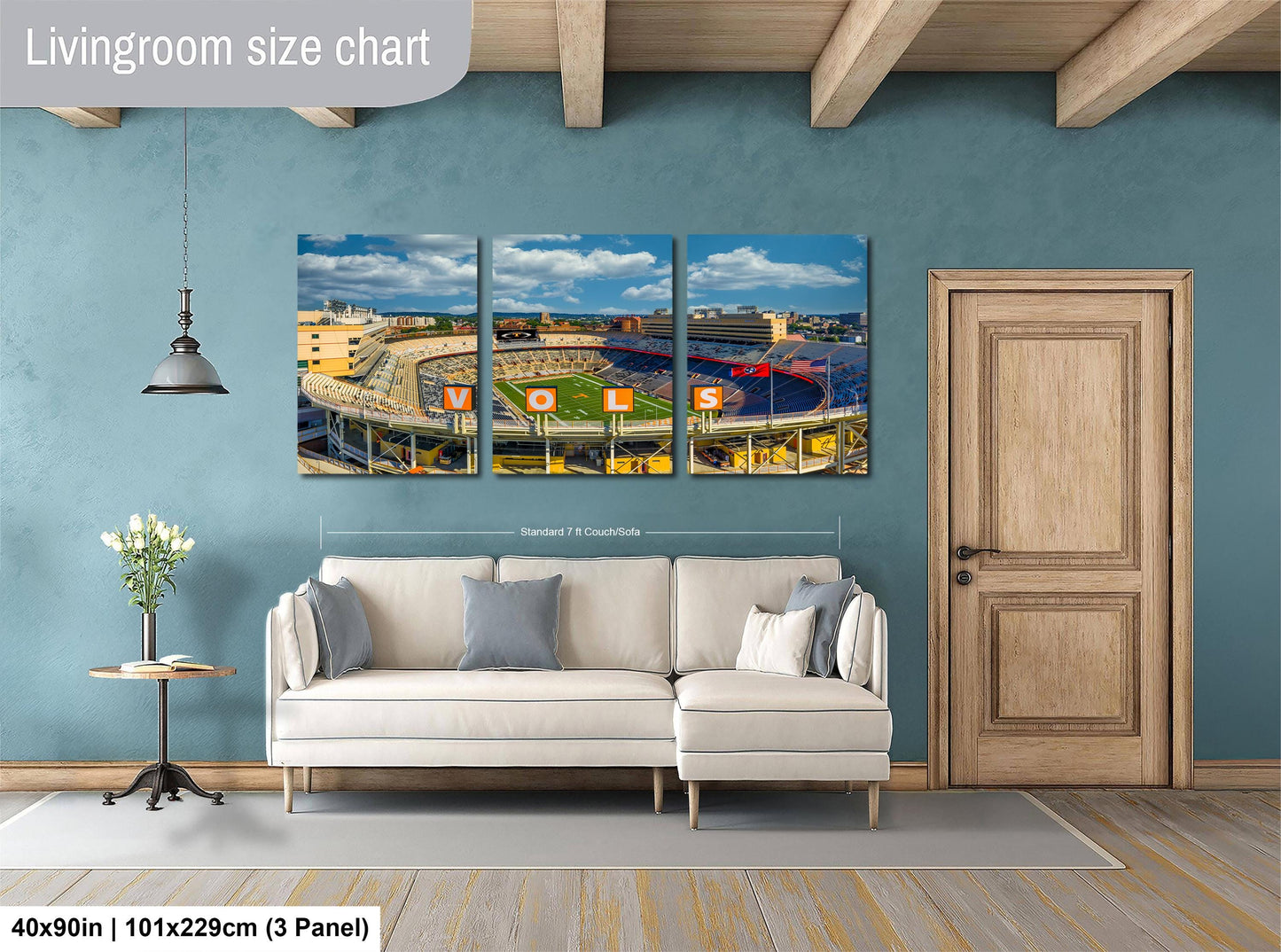 The image is a living room with a large wall art depicting a stadium scene. The wall art is divided into three panels, each showing different parts of the stadium. The living room has a white sofa and a wooden door.