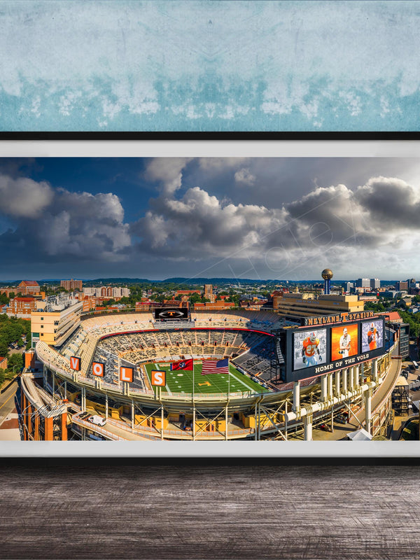 The image is a framed photograph of a football stadium with a city skyline in the background.