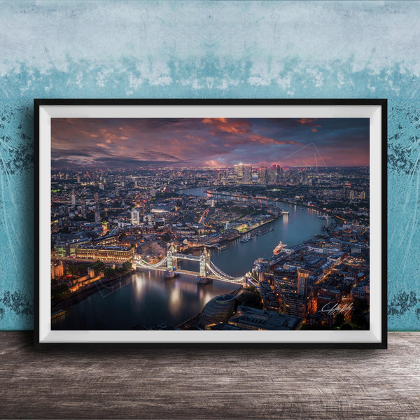 The image is a framed aerial view of a city at night, showcasing a bridge and the city skyline with illuminated buildings and a river.