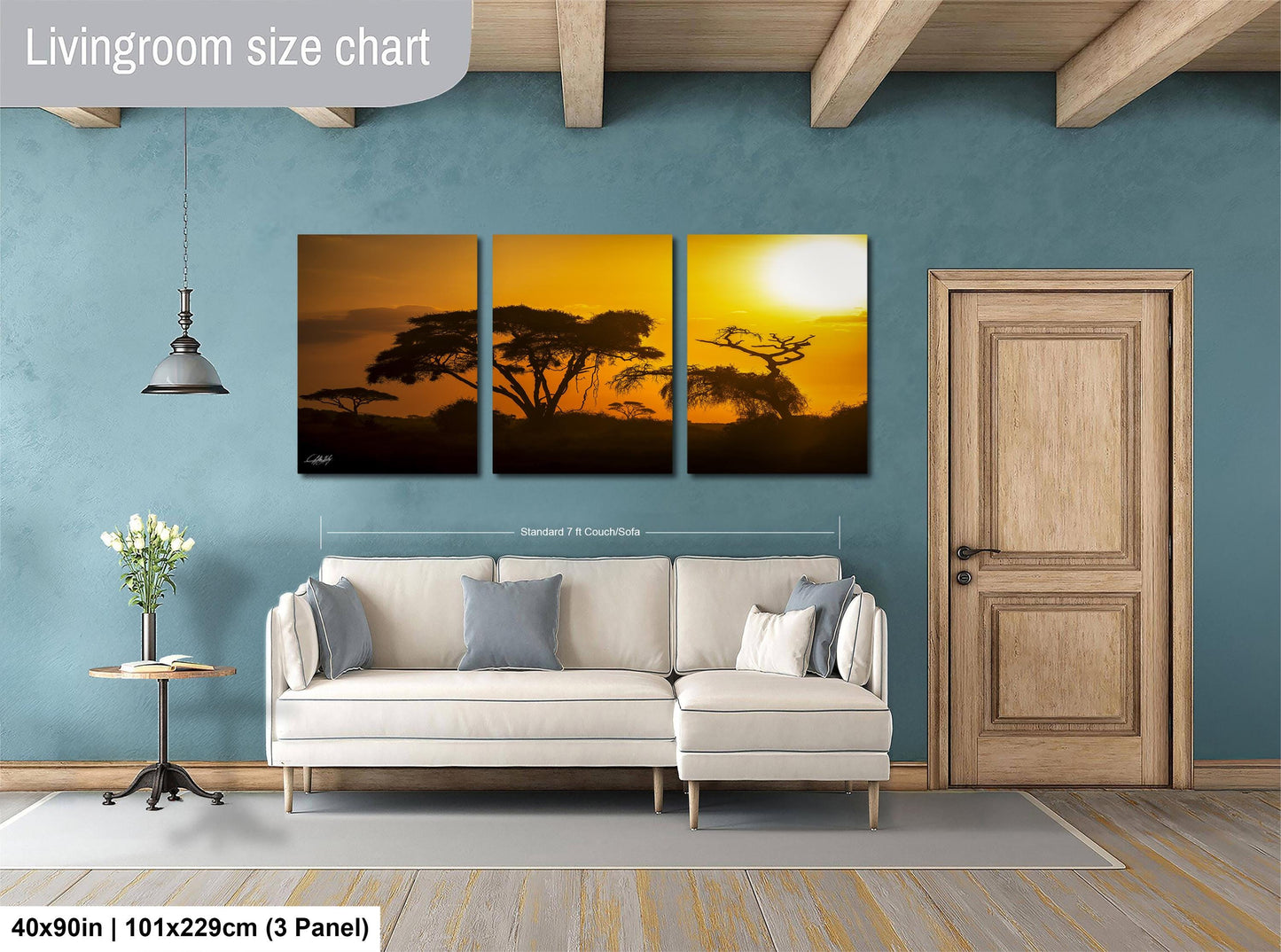 The image is a living room with a large wall art piece depicting a sunset over a landscape. The art piece is divided into three panels, each showing different aspects of the sunset. The living room has a white sofa and a wooden door, creating a cozy and inviting atmosphere.