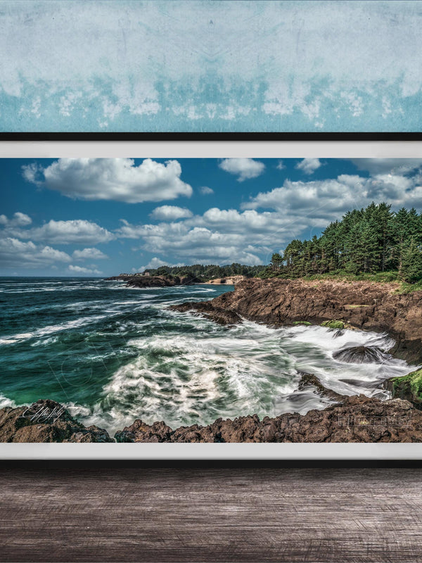 A framed photograph of a rocky coastline with crashing waves, set against a backdrop of a blue sky with fluffy white clouds.