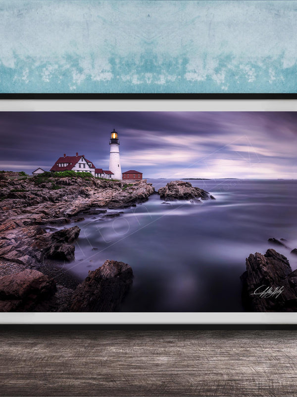A framed photograph of a lighthouse on a rocky shore, with the ocean and a cloudy sky in the background.