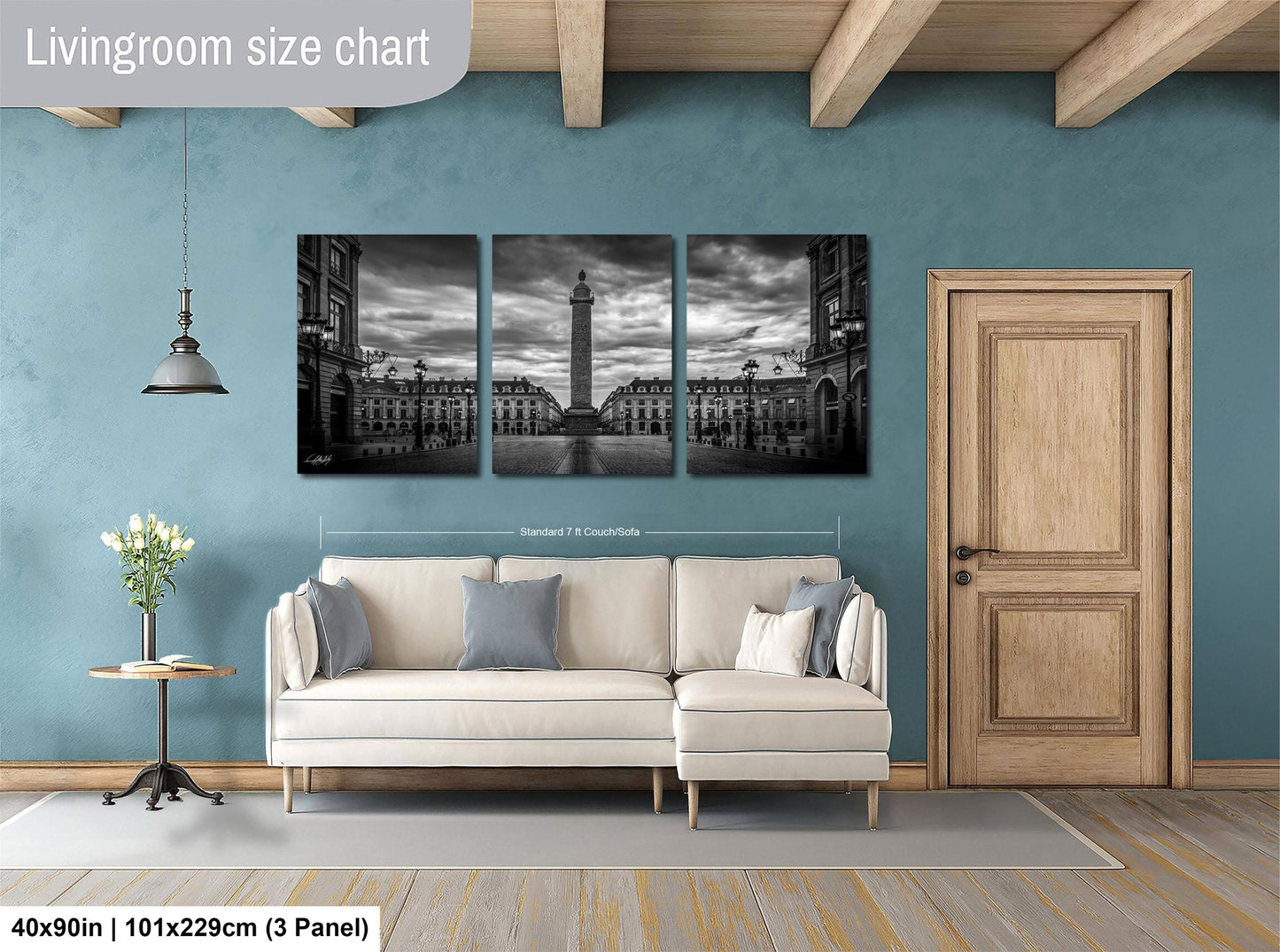 The image is a living room with a large, three-panel black and white landscape painting hanging on the wall. The painting depicts a cityscape with a tall tower in the center. The room has a white sofa, a wooden door, and a small table with a vase of flowers. The wall is painted in a light blue color, and the floor is covered with a gray rug.