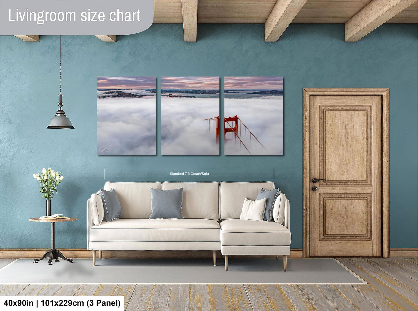 The image is a living room with a large, three-panel wall art depicting a scenic view of the Golden Gate Bridge and the foggy landscape below. The wall art is framed by a wooden door and a white sofa, creating a cozy and inviting atmosphere.