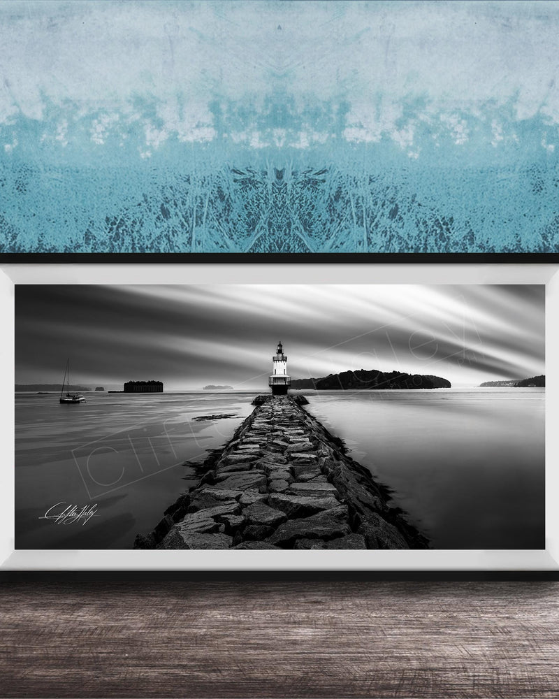 A black and white photograph of a lighthouse on a rocky pier, with a calm body of water and a cloudy sky in the background.