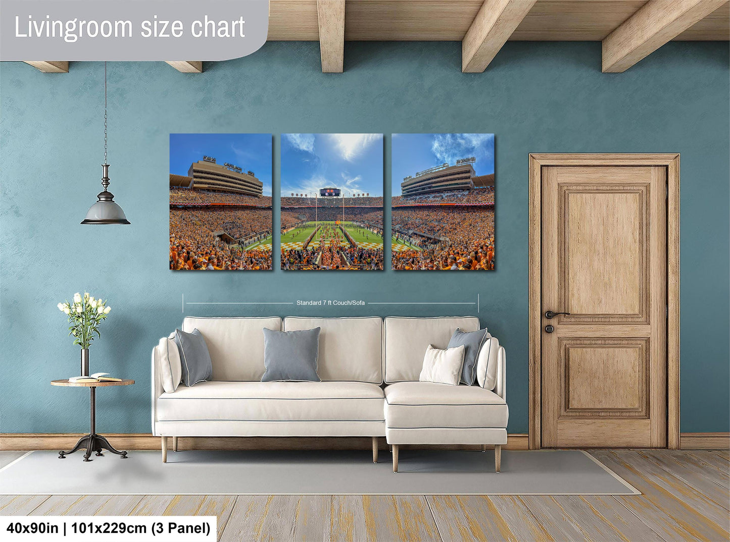 The image is a living room with a large wall-mounted painting depicting a crowded stadium. The painting is divided into three panels, each showing different parts of the stadium. The wall is painted a light blue color, and there is a wooden door and a white sofa in the room.