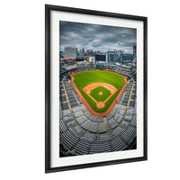 An aerial view of a baseball stadium with a green field, brown dirt infield, and rows of empty seats. The stadium is surrounded by a city skyline, and the sky is cloudy.