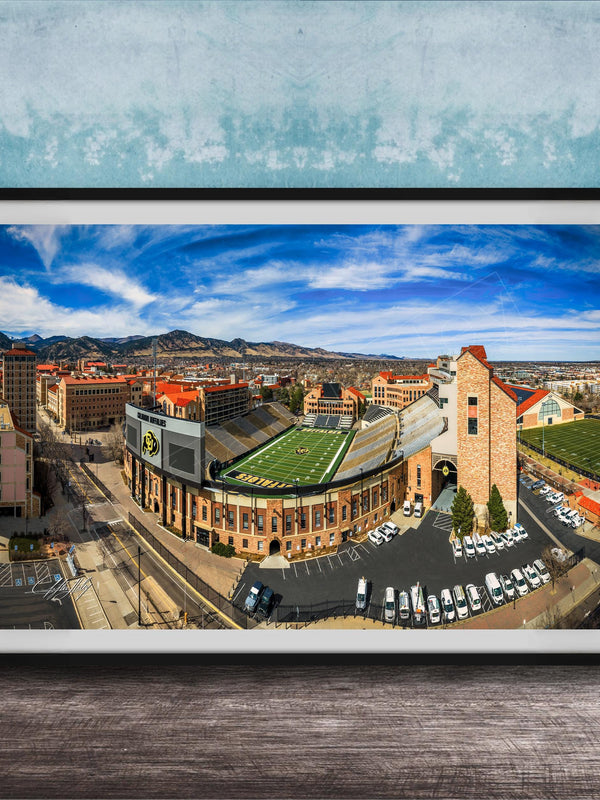 The image is a framed aerial view of a city, featuring a football stadium, buildings, and a parking lot.