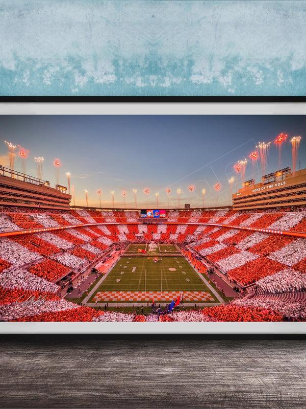 A framed photograph of a football stadium at night, with the field illuminated by red and white lights and the stands filled with spectators.