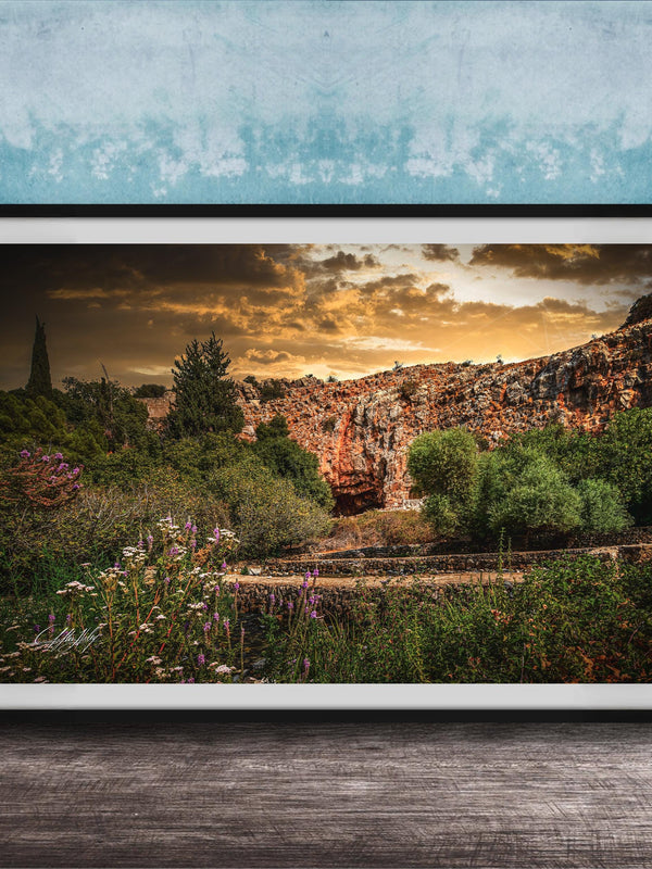 The image is a framed photograph depicting a scenic landscape with a rocky cliff, lush vegetation, and a dramatic sky with clouds.
