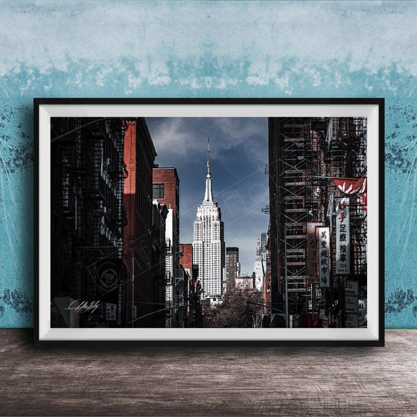 A framed photograph of the iconic Empire State Building in New York City, with the surrounding cityscape visible through the glass facade.