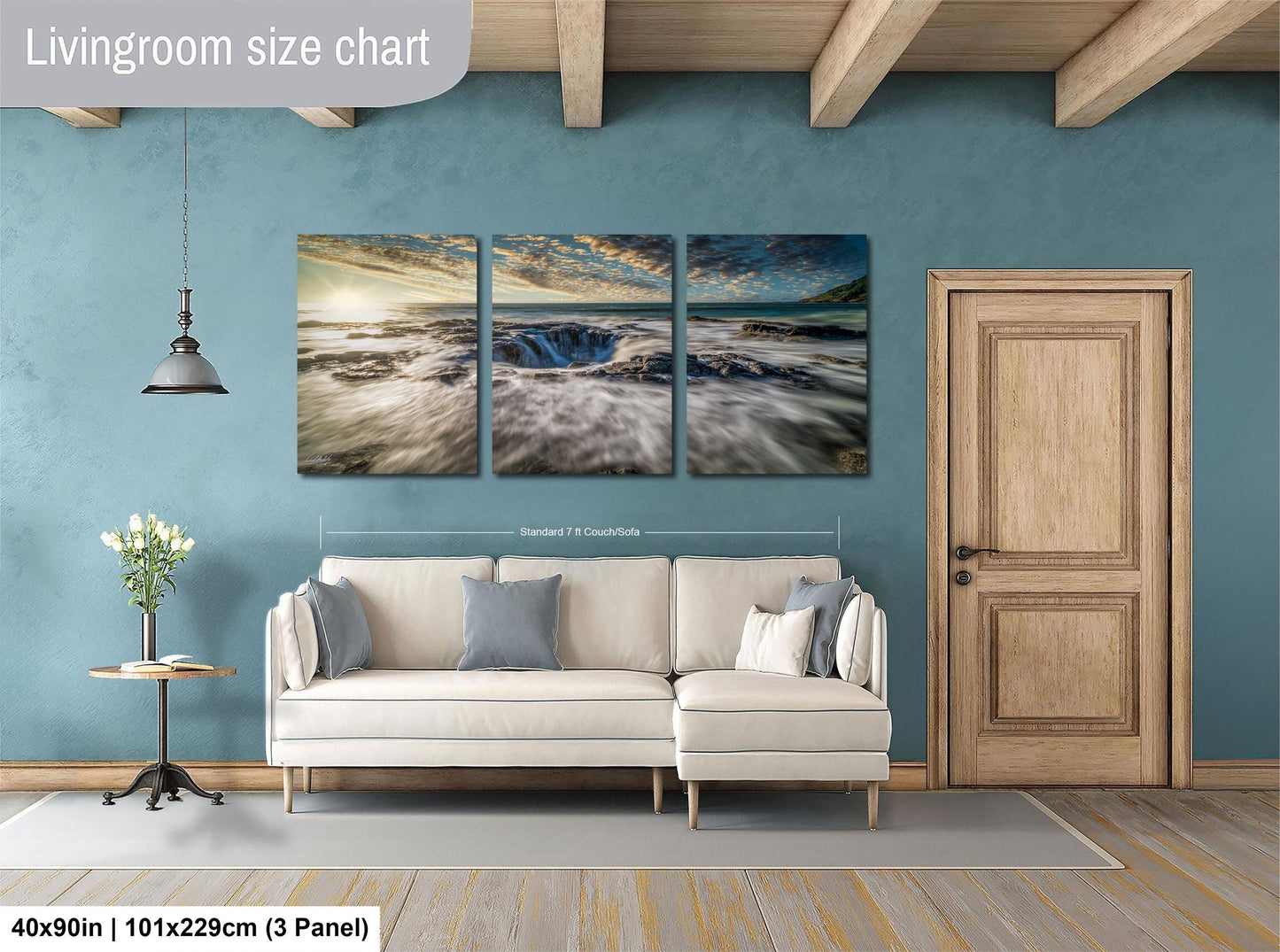 The image is a living room with a large, three-panel landscape painting hanging on the wall. The painting depicts a serene beach scene with a blue sky, ocean, and clouds. The room is furnished with a white sofa and a wooden door, creating a cozy and inviting atmosphere.