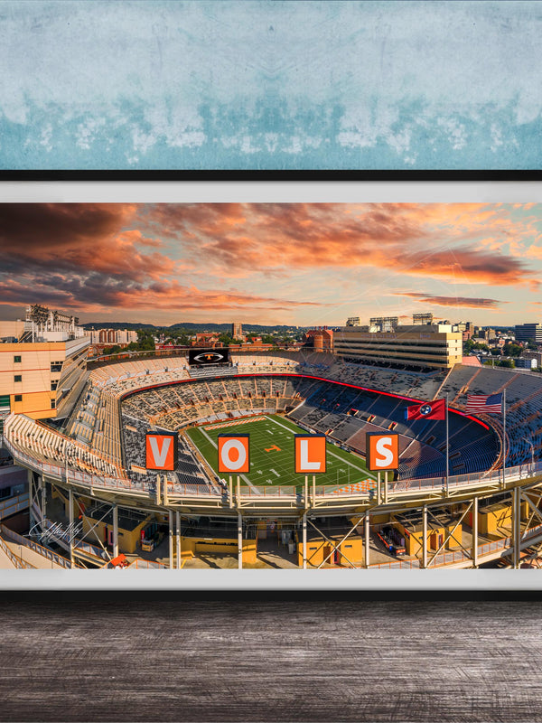 A framed photograph of a sports stadium with the word "VOLS" prominently displayed, set against a backdrop of a colorful sunset sky.