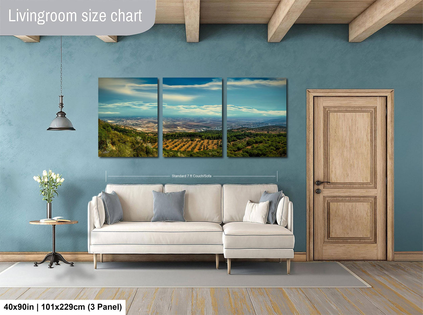 The image is a living room with a large wall art depicting a scenic landscape with mountains, fields, and a blue sky. The living room has a white sofa, a wooden door, and a wooden floor.