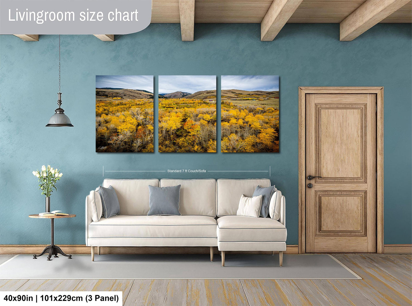 The image is a livingroom with a large wall-mounted painting depicting a scenic landscape with a field of yellow flowers. The painting is divided into three panels, and the wall is painted a light blue color. The living room has a white sofa and a wooden door, and there is a small table with a vase of flowers nearby. The image is described as a "Livingroom size chart" and includes dimensions and a scale of "40x50 inches (101x129 cm) (3 panel)".