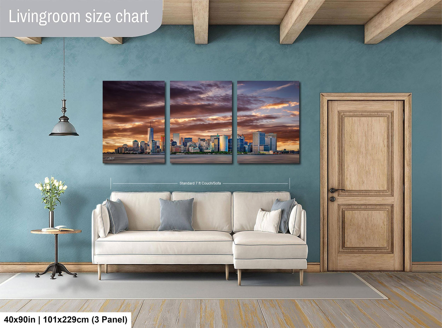 The image is a living room with a large wall art depicting a city skyline at sunset. The wall art is divided into three panels, each showing a different part of the cityscape. The room has a white sofa, a wooden door, and a wooden floor. The wall art is approximately 40 inches wide and 101.29 cm tall, with a 3-panel layout.