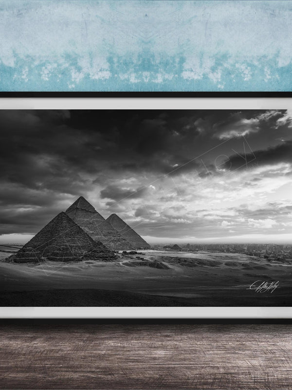 A black and white photograph of the iconic pyramids of Giza in Egypt, set against a dramatic cloudy sky.