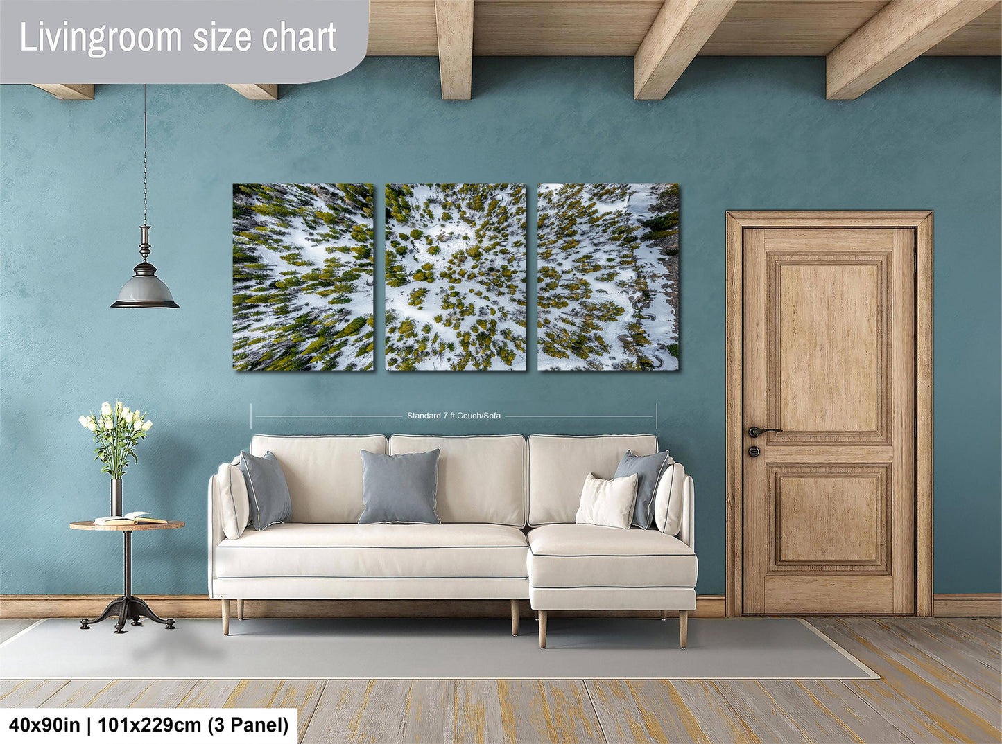 The image is a living room with a white sofa, a wooden door, and a large wall art depicting a snowy landscape with trees.