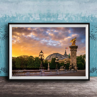 a picturesque scene of a cityscape with a large domed building, ornate lampposts, and a statue of a winged figure, all set against a vibrant sunset sky.